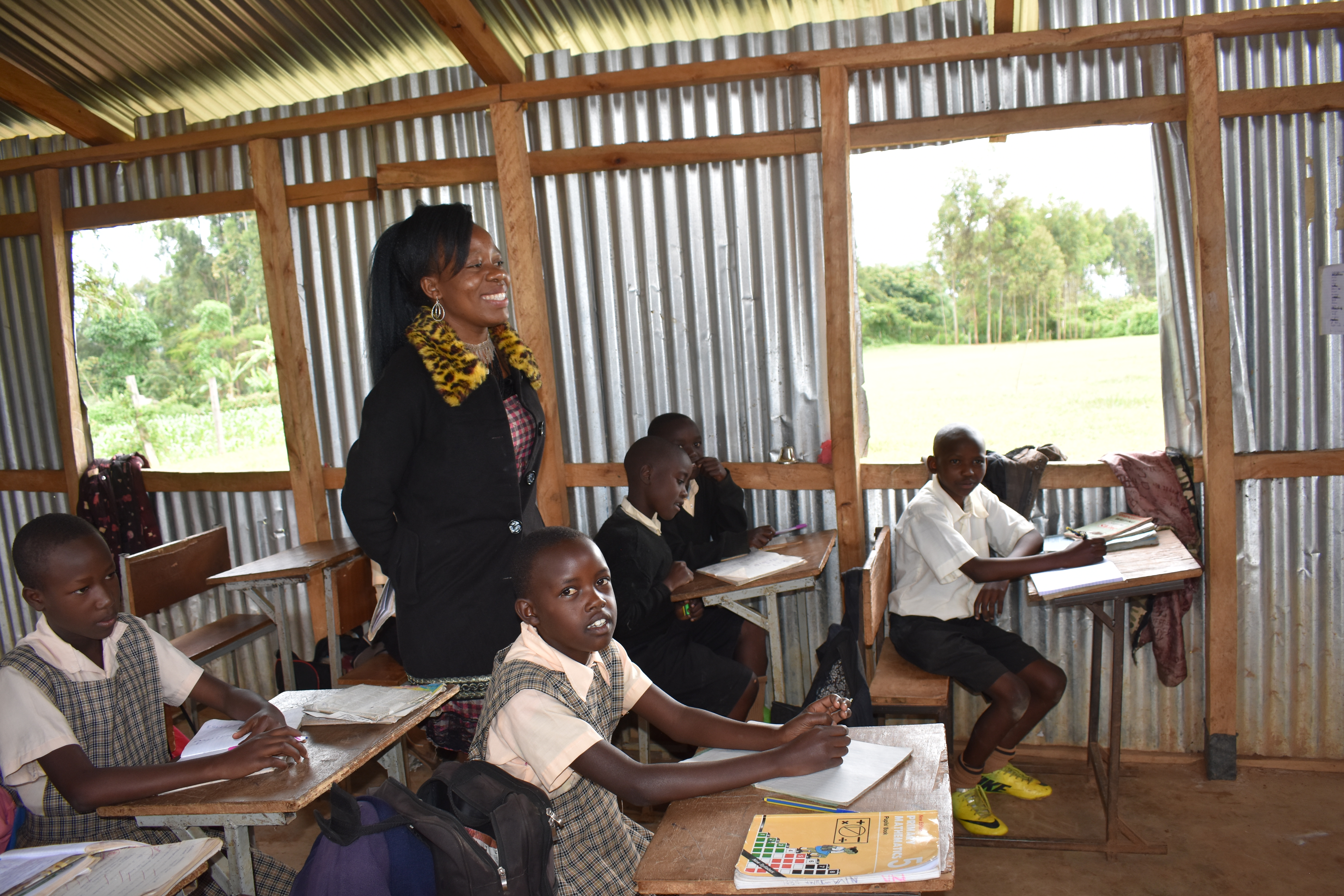 A Kenyan teacher walks between rows of students inside her classroom.
