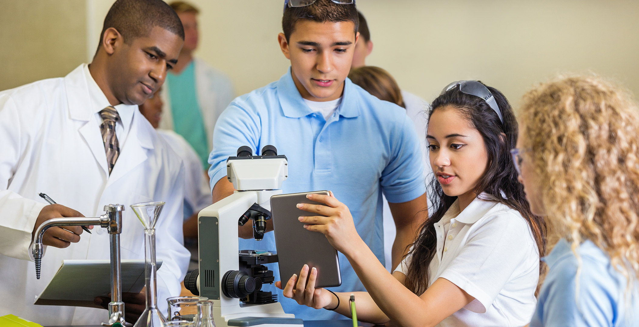 A group of students gather around a microscope.