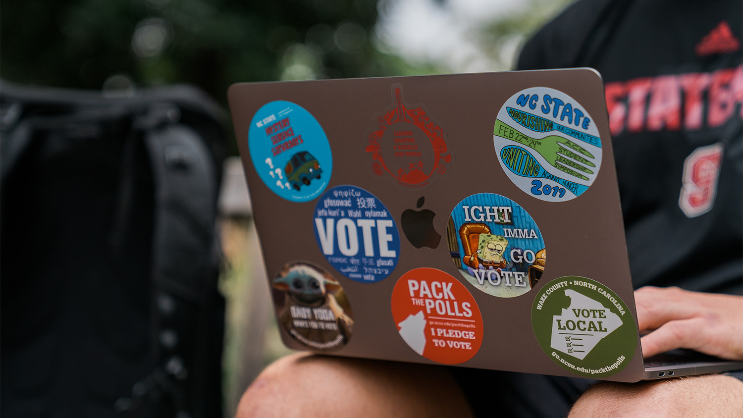 Hands typing on a laptop covered in stickers related to voting