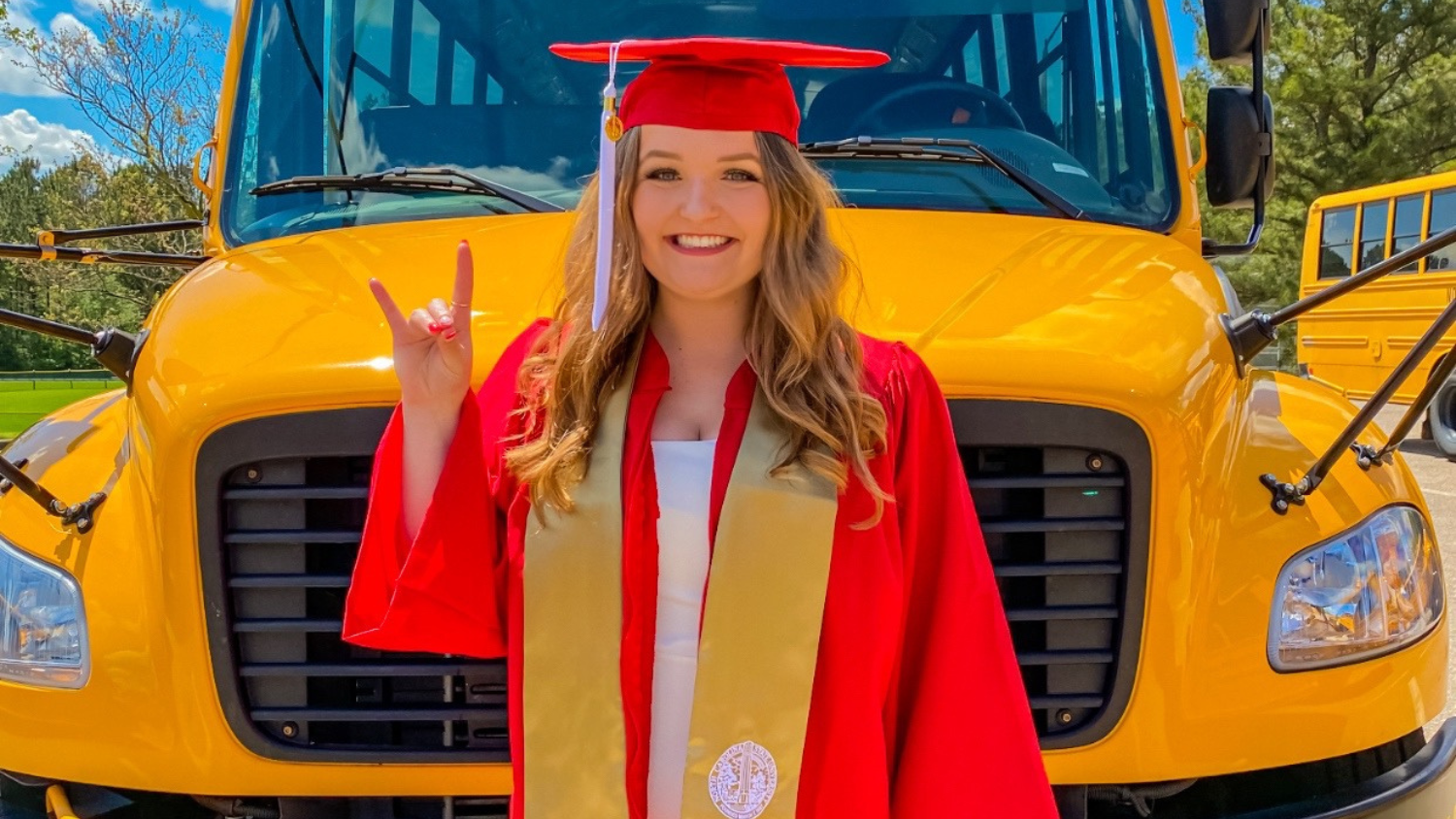Kailee Storie in cap and gown standing in front of a school bus.