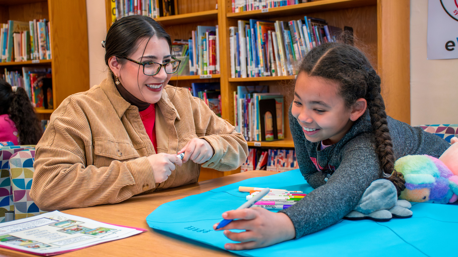 A College of Education Student helping an elementary school student at a school