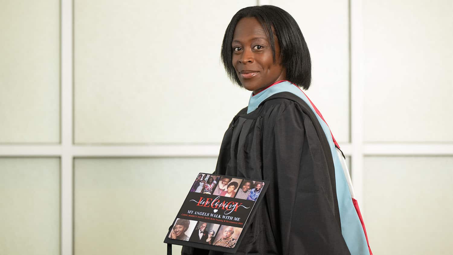 Carol Davis holding her graduation cap, which is decorated with photos of family members who inspired her