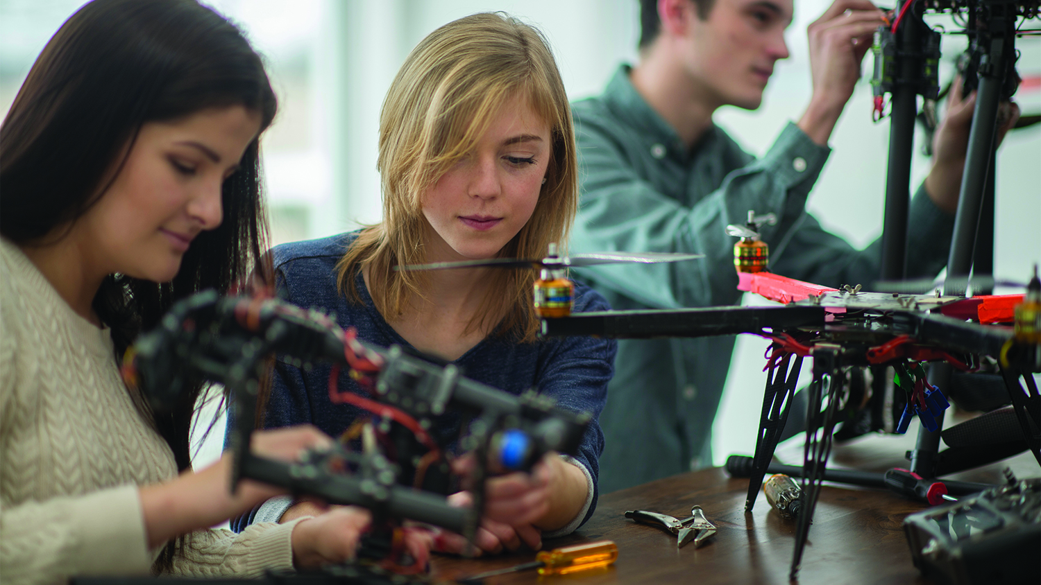 A group of college students are working on the mechanics for a robotics and drone project in university.