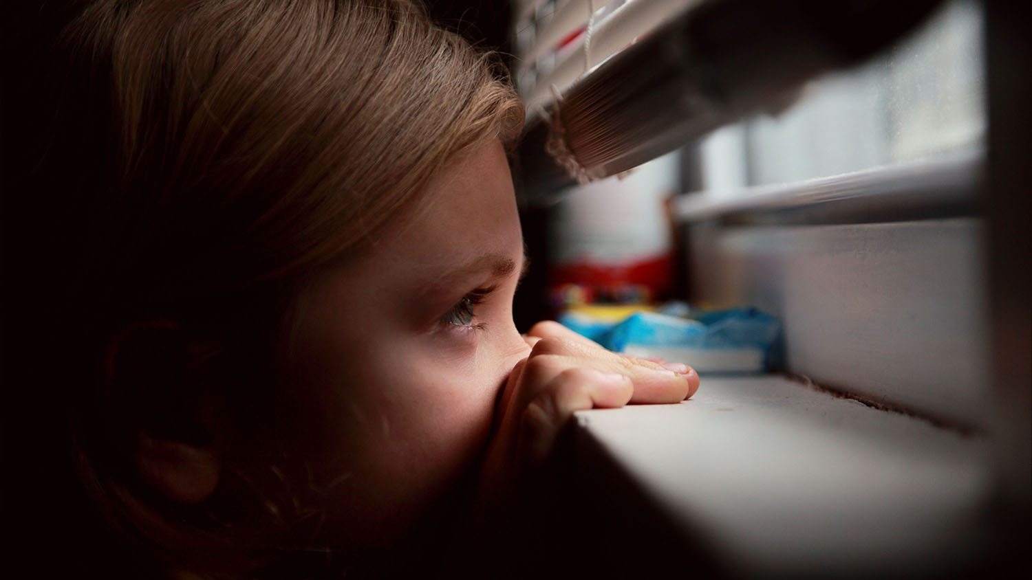 A young child peering through the bottom of a closed window
