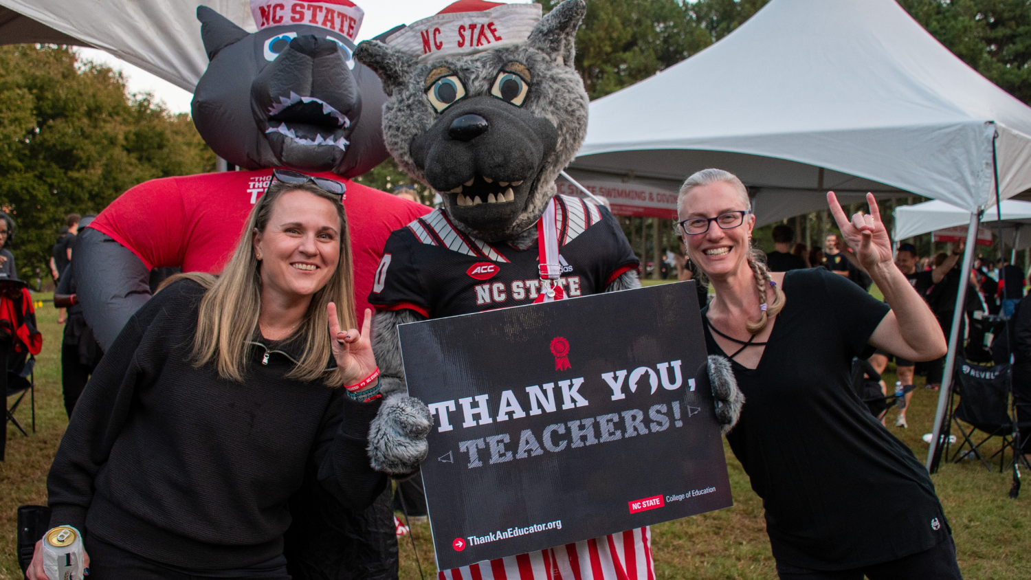 Two women standing with Mr. Wuf, who is holding a sing that reads 